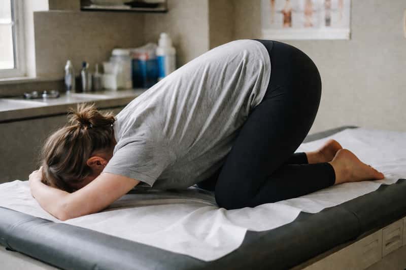 Person in knee-chest position on exercise mat, forehead resting on folded arms, knees bent beneath torso, demonstrating medic