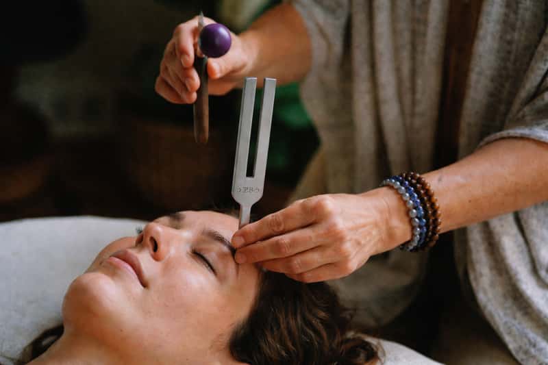 A silver tuning fork vibrating beside a hand, soft window A silver tuning fork vibrating beside a hand, soft window light on a wooden table.